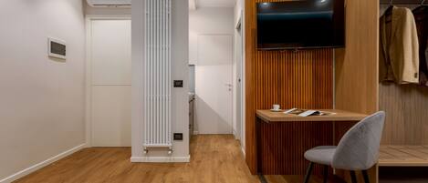 Une chambre moderne avec un plancher en bois, un radiateur blanc, un bureau avec une chaise, un téléviseur fixé au mur et un portant à vêtements.
