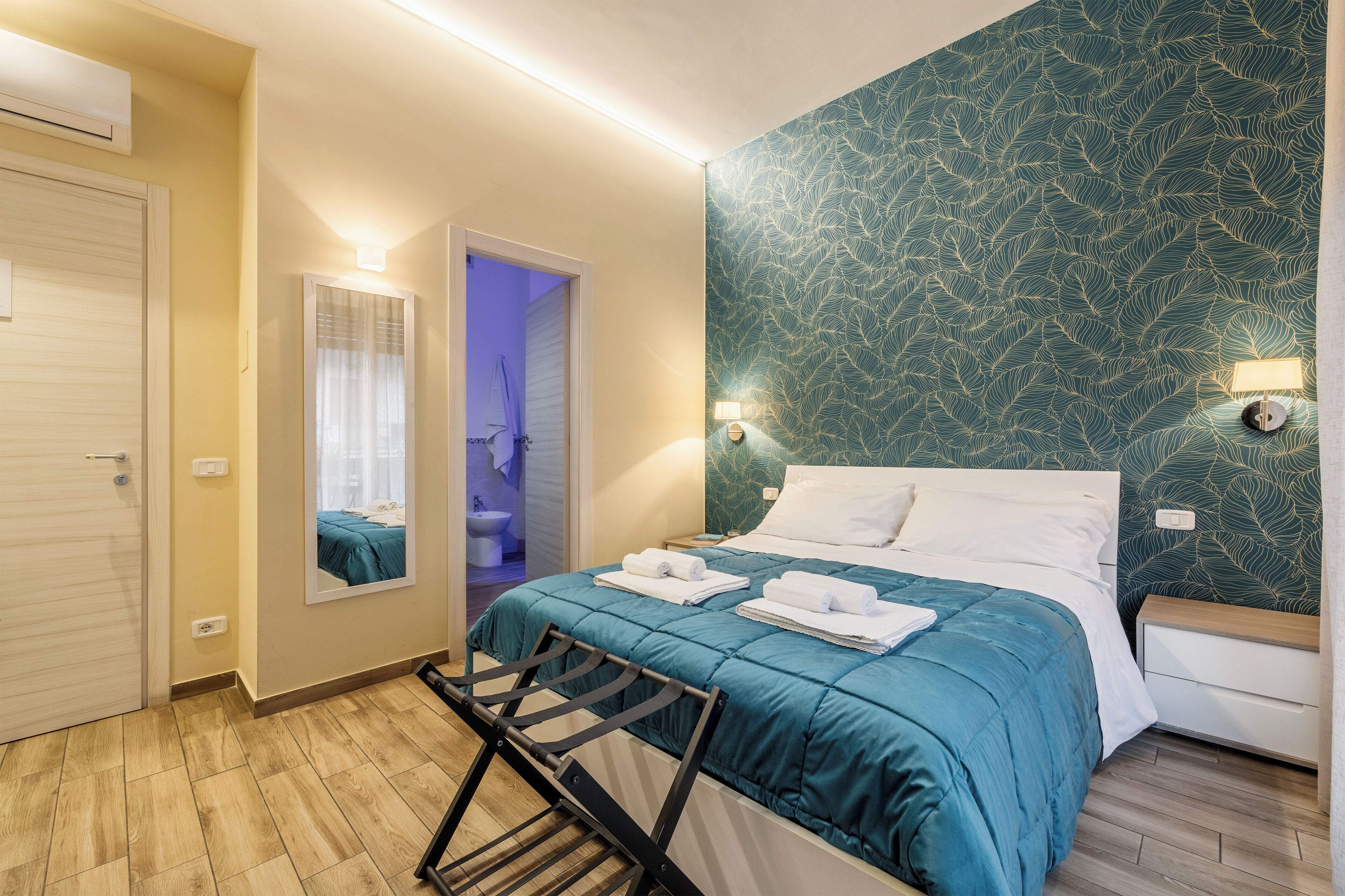 Habitación de hotel con cama, espejo, puerta de baño y pared con diseño de hojas.