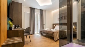A modern hotel room with a wooden desk, a bed with a headboard, a seating area with a chair, and a glass partition. - Quinto Stabile Rooms&Suite (Palermo)