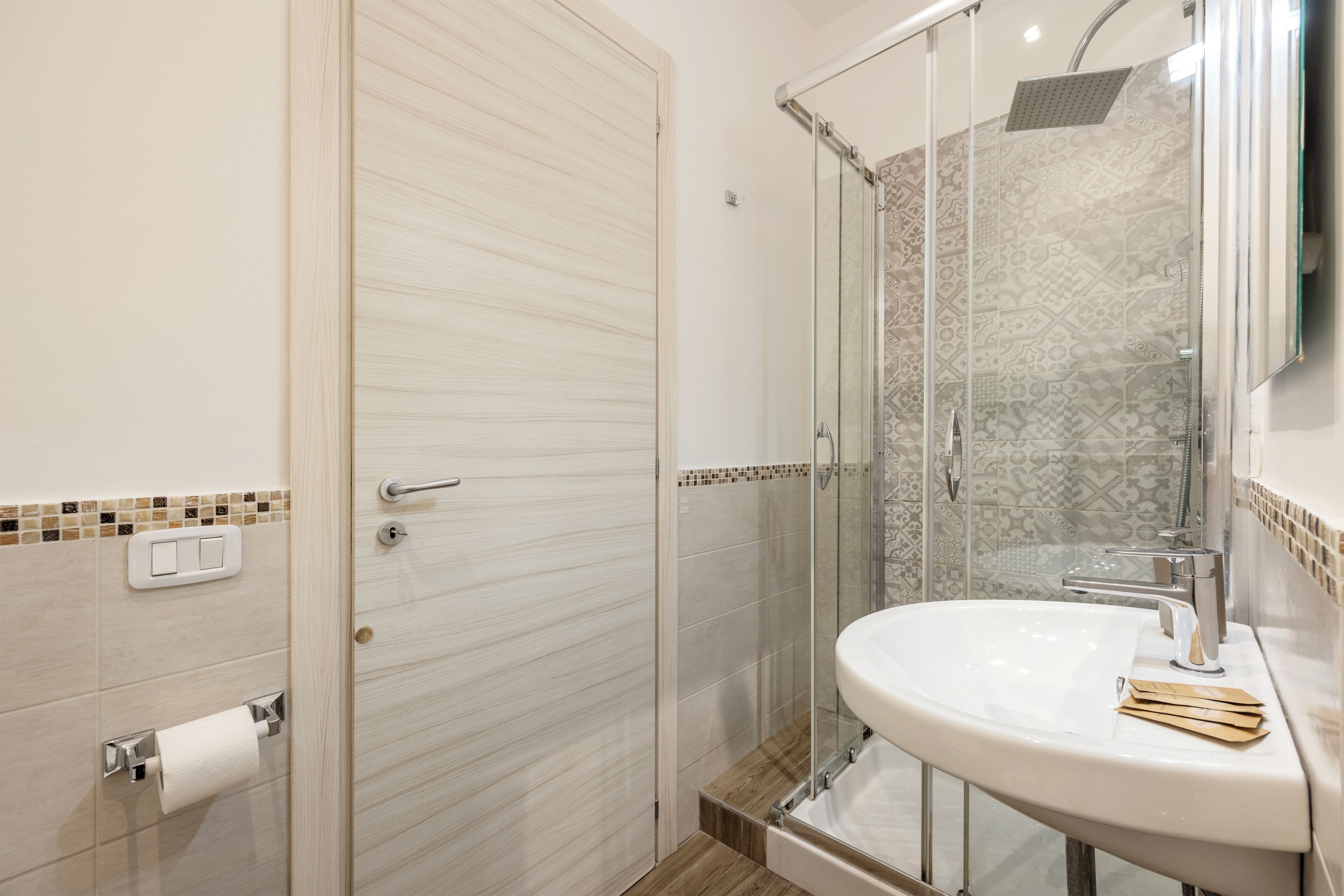 Un bagno moderno con cabina doccia in vetro, un lavandino bianco e un portasciugamani.