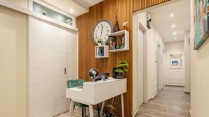 A modern hallway with a wooden accent wall, a white desk with a globe, a clock, and shelves with books and decorative items. - Quinto Stabile Rooms&Suite (Palermo)