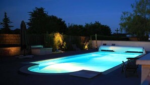Uma piscina com borda curva, rodeada por espreguiçadeiras e uma área coberta.