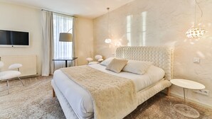 Quarto moderno com cama grande, televisão de tela plana, mesinha e luminária de design exclusivo.