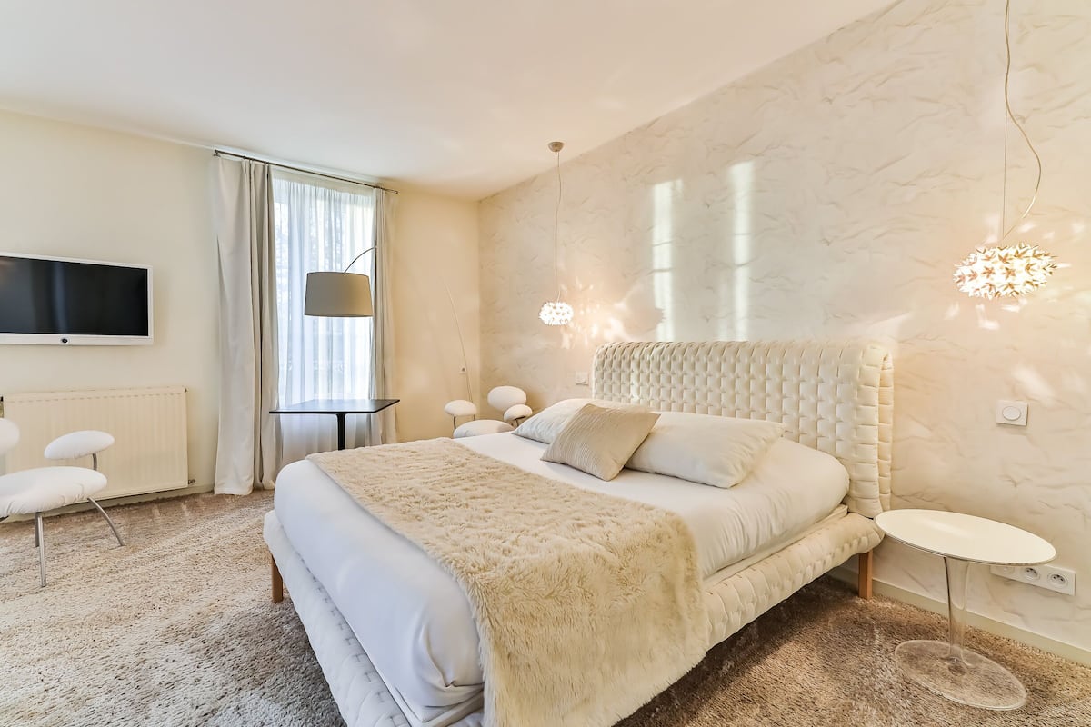 Un dormitorio moderno con una cama grande, un televisor de pantalla plana, una mesita pequeña y una lámpara de techo original.