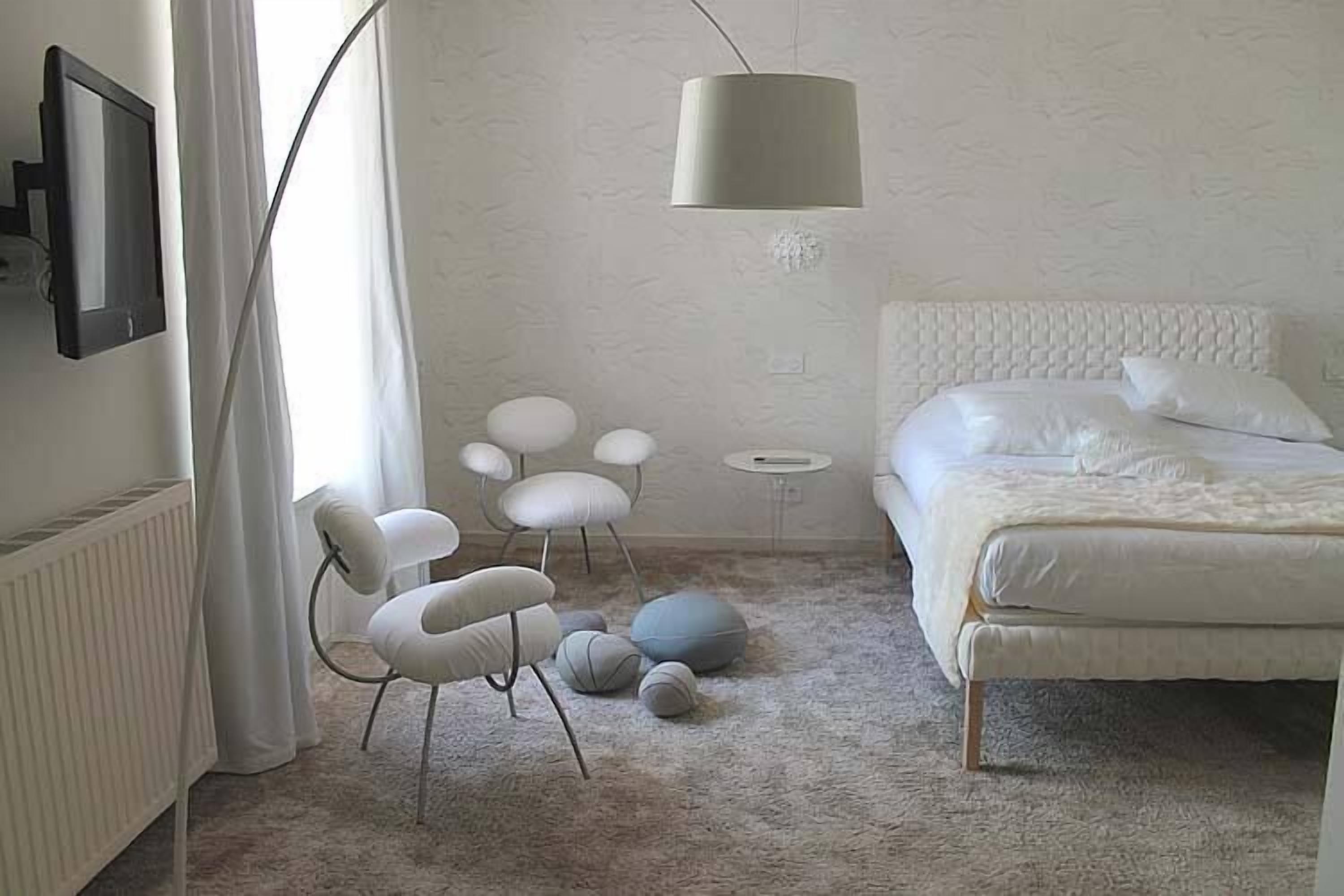 Un dormitorio con una cama, una silla, una lámpara y un radiador.