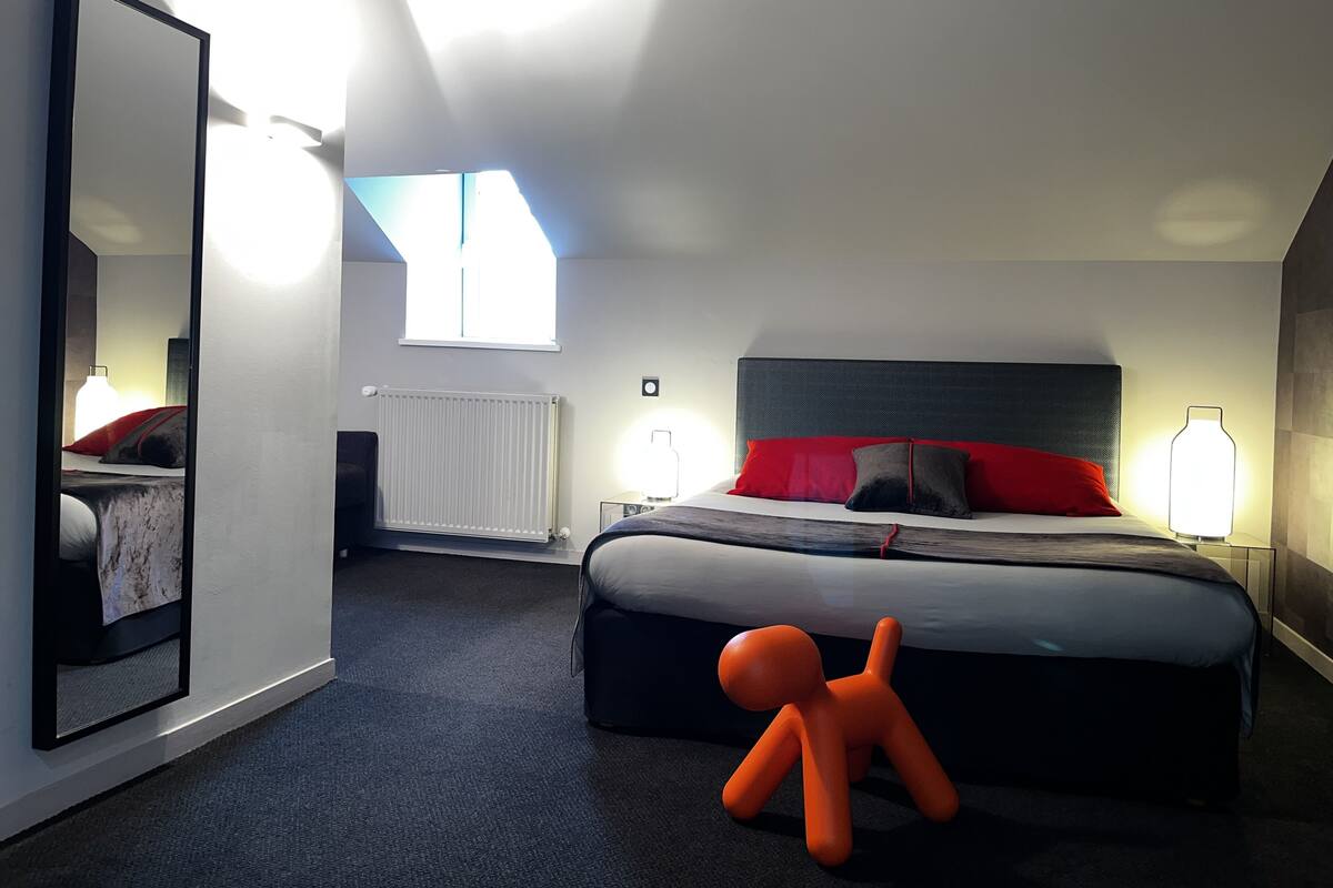 Una habitación de hotel moderna con una cama grande, una mesita de noche, un espejo y una ventana.