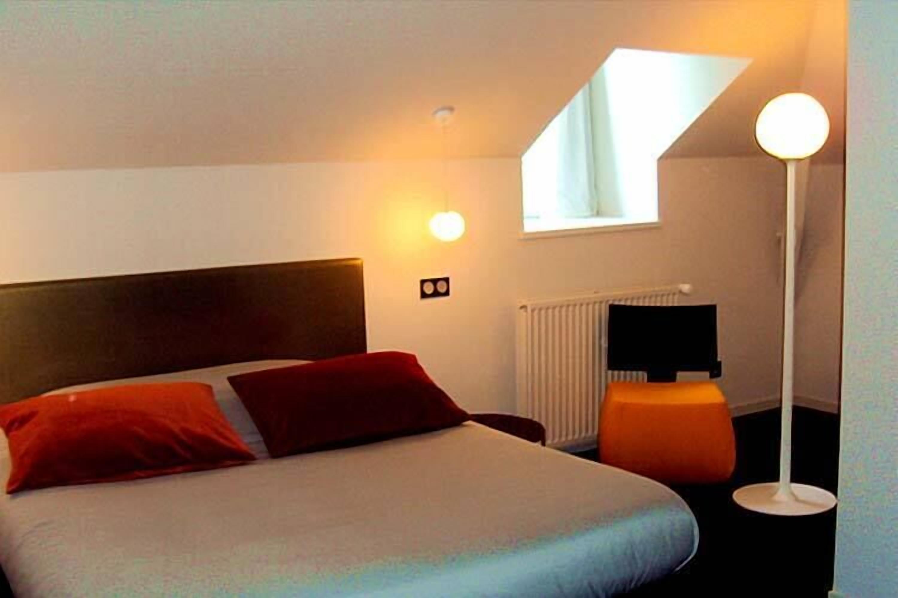 A hotel room with a bed, a nightstand, a lamp, a window, and a radiator.