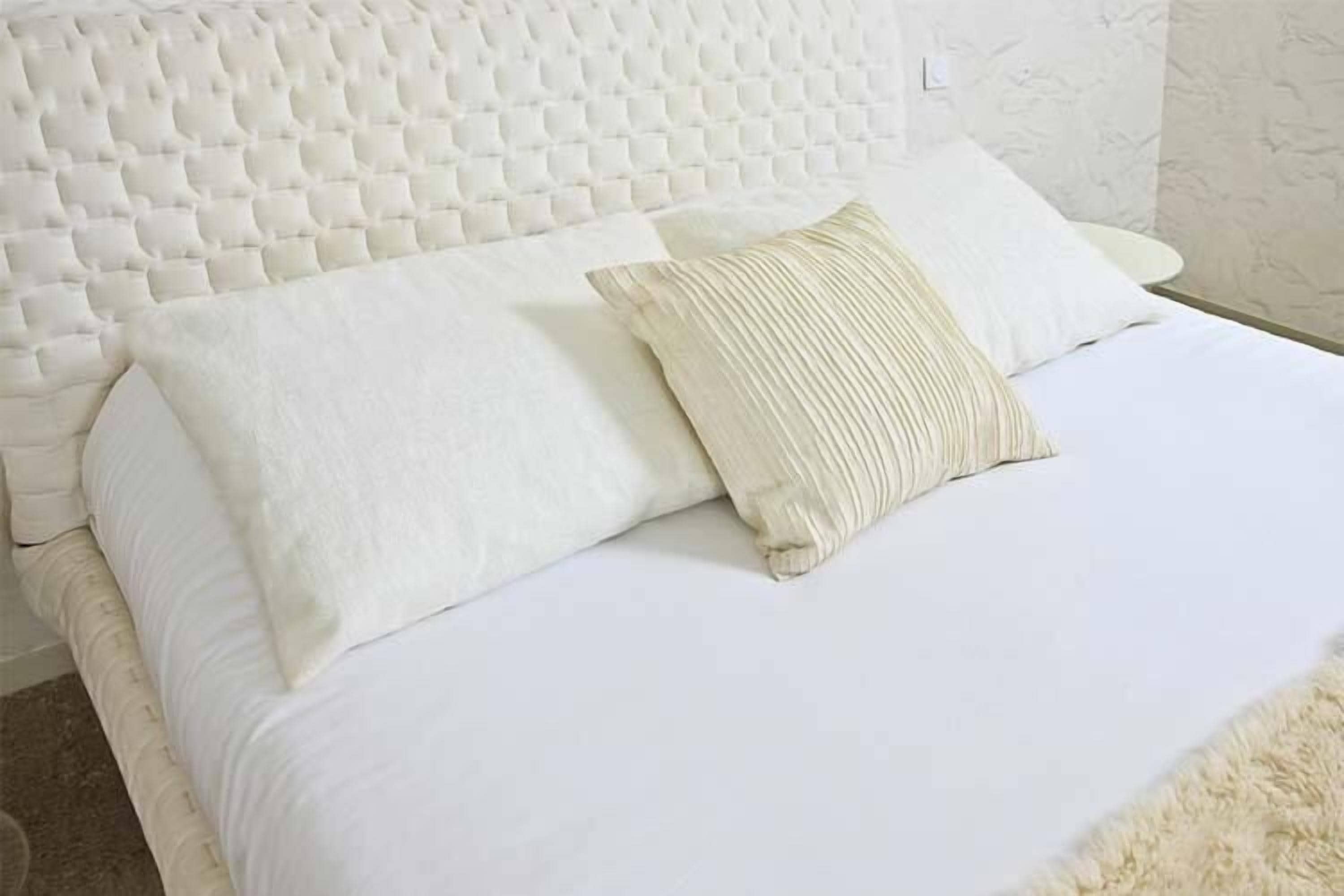 A neatly made bed with a tufted headboard, white bedding, and a fluffy rug.