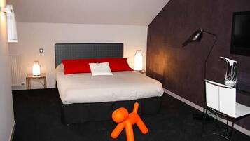 A modern hotel room with a large bed, red and white bedding, a black headboard, a desk with a chair, and a television on the wall.