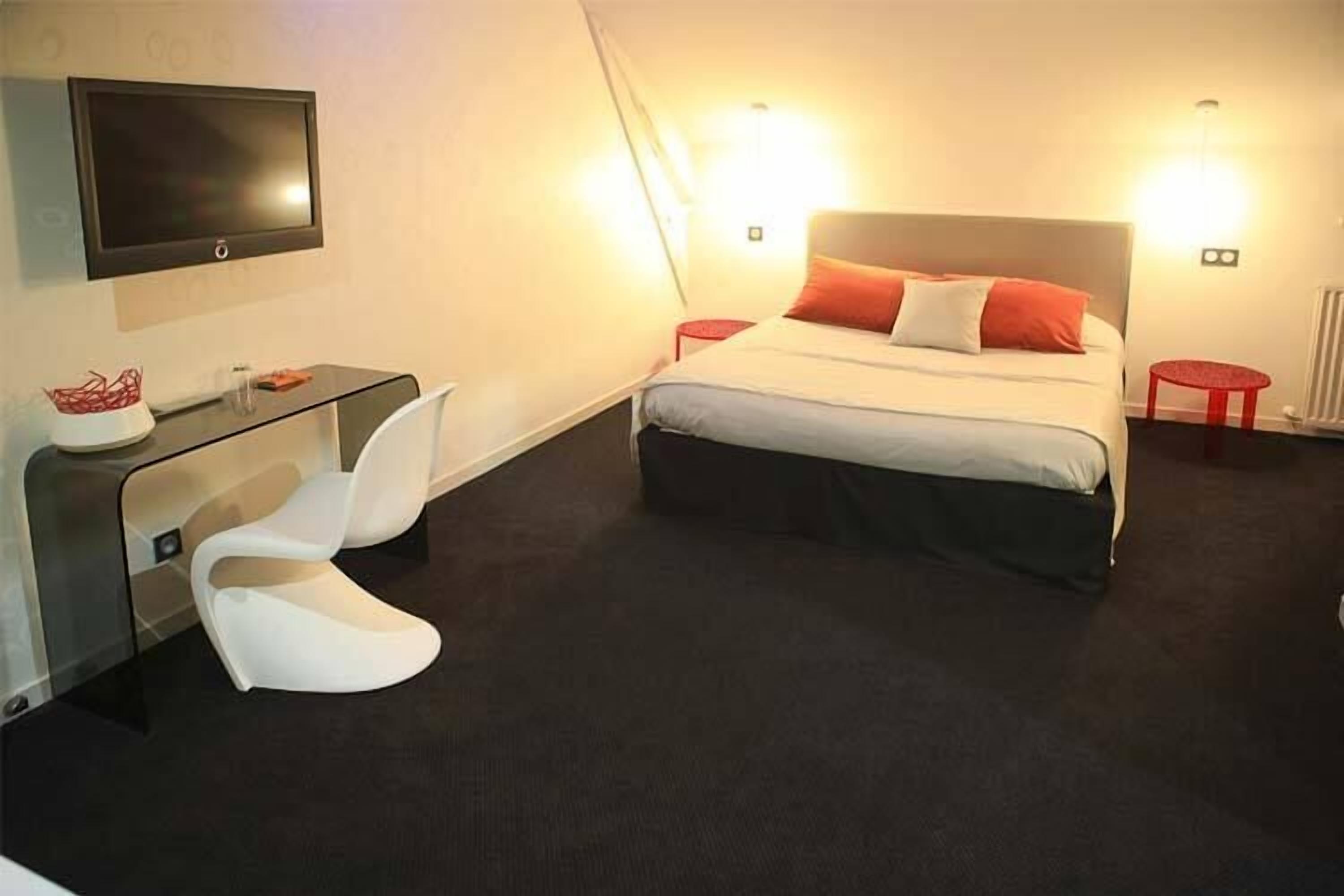 Een moderne hotelkamer met een bed, een aan de muur bevestigde televisie, een bureau met een stoel en een klein krukje.