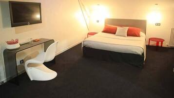 Een moderne hotelkamer met een bed, een aan de muur bevestigde televisie, een bureau met een stoel en een klein krukje.