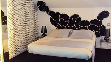 A modern bedroom with a geometric wall art, a bed with white bedding, and a side table with a lamp.