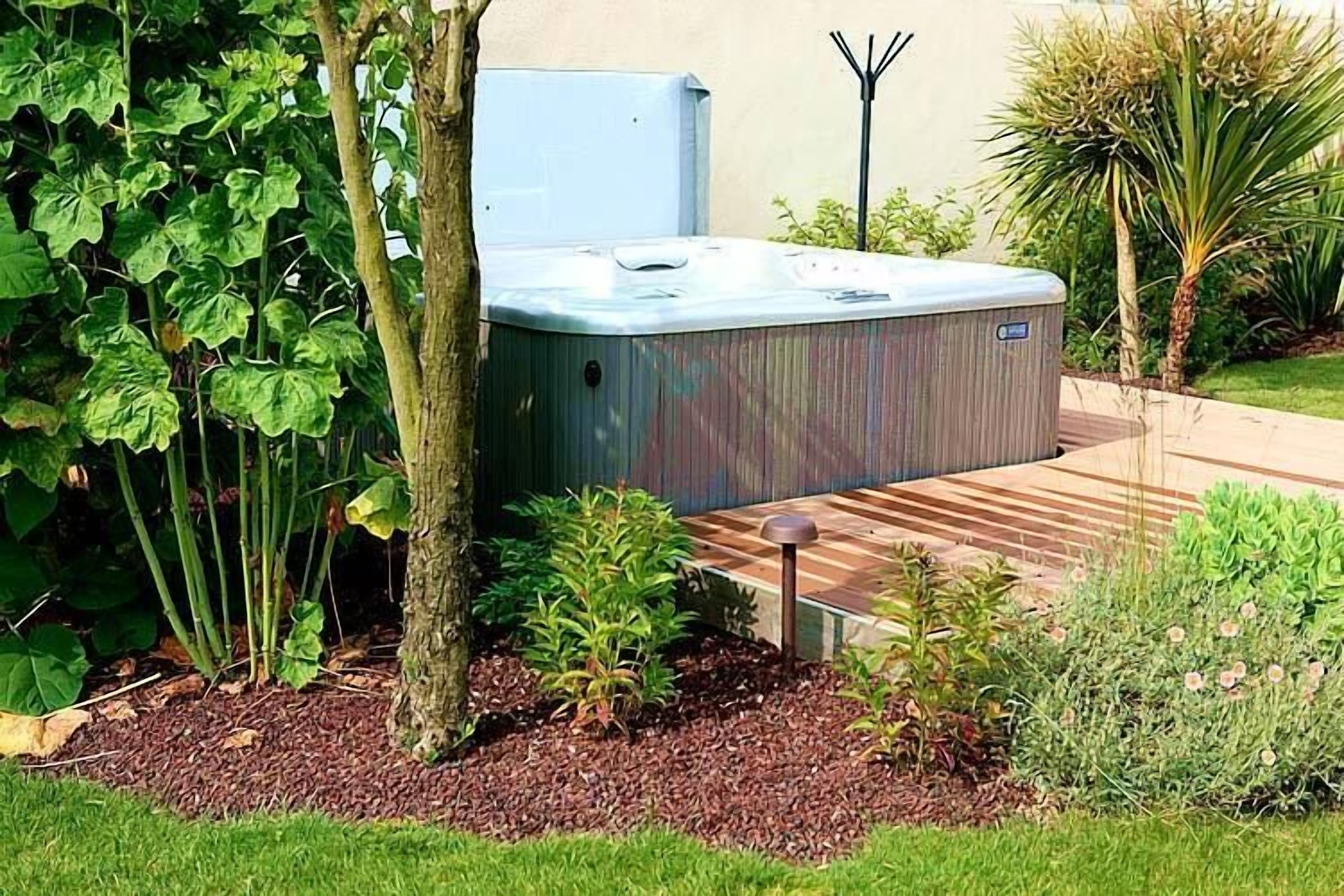 A hot tub in a landscaped garden with a wooden deck and various plants.