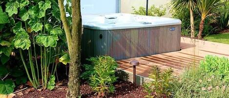 A hot tub in a landscaped garden with a wooden deck and various plants.