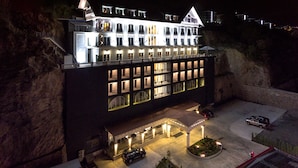 A multi-story hotel with a balcony on the upper level, a covered entrance, and a parking area with cars. - Mell Hotel (Trabzon)