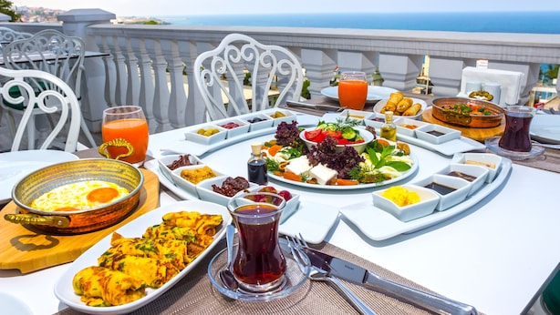 A table set for breakfast with various dishes, a glass of orange juice, and a view of the sea. - Mell Hotel (Trabzon)