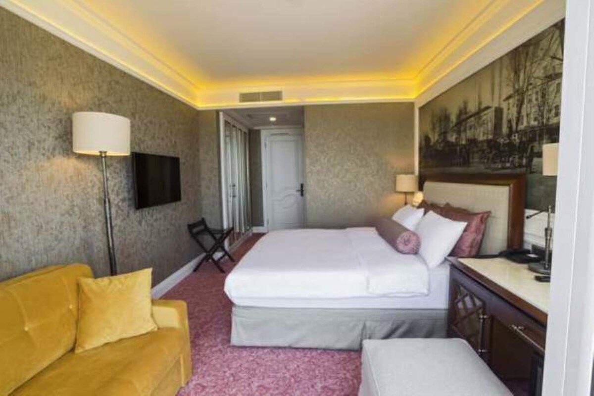 A hotel room with a bed, a sofa, a television, and a painting on the wall.