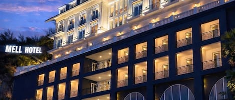 Un hotel de varios pisos con balcones, una entrada bien iluminada y un cartel que dice 'MELL HOTEL'.