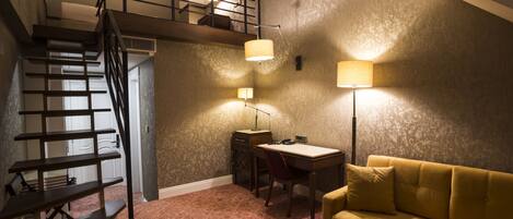 A room with a staircase, a desk, a yellow sofa, and two wall-mounted lamps.