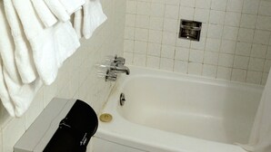 A bathroom with a bathtub, a towel rack with white towels, a handheld showerhead, and a window with frosted glass. - Chalet Inn Motel (Dryden)