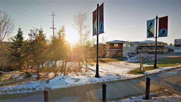 A motel with a parking lot, a building with a garage, and a flagpole with flags. - Chalet Inn Motel (Dryden)