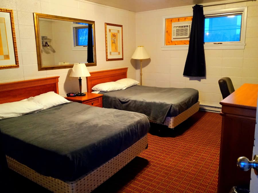 Una habitación de hotel con dos camas, una mesita de noche con lámpara, un aparador y una ventana con cortina.