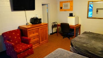 Hotelkamer met een enkel bed, een rode fauteuil, een houten dressoir, een bureau met stoel, een aan de muur bevestigde televisie en een raam met houten kader.