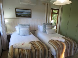 Dos camas individuales con ropa de cama a rayas, un cuadro en la pared y una ventana con cortinas.