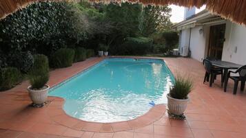 Relax by the serene pool surrounded by lush gardens and a shaded patio area.