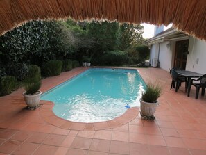 Relax by the serene pool surrounded by lush gardens and a shaded patio area.