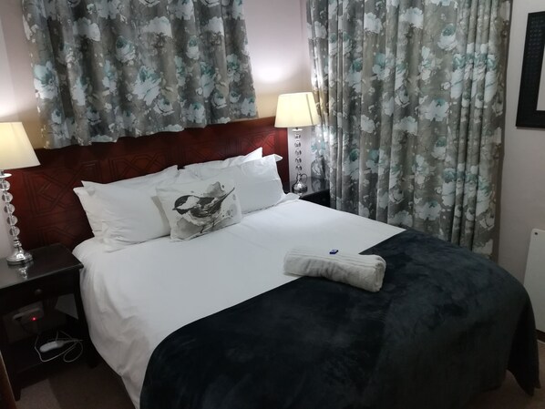 Restful retreat with a neatly made bed, featuring a white duvet and throw blanket, and a bedside lamp.
