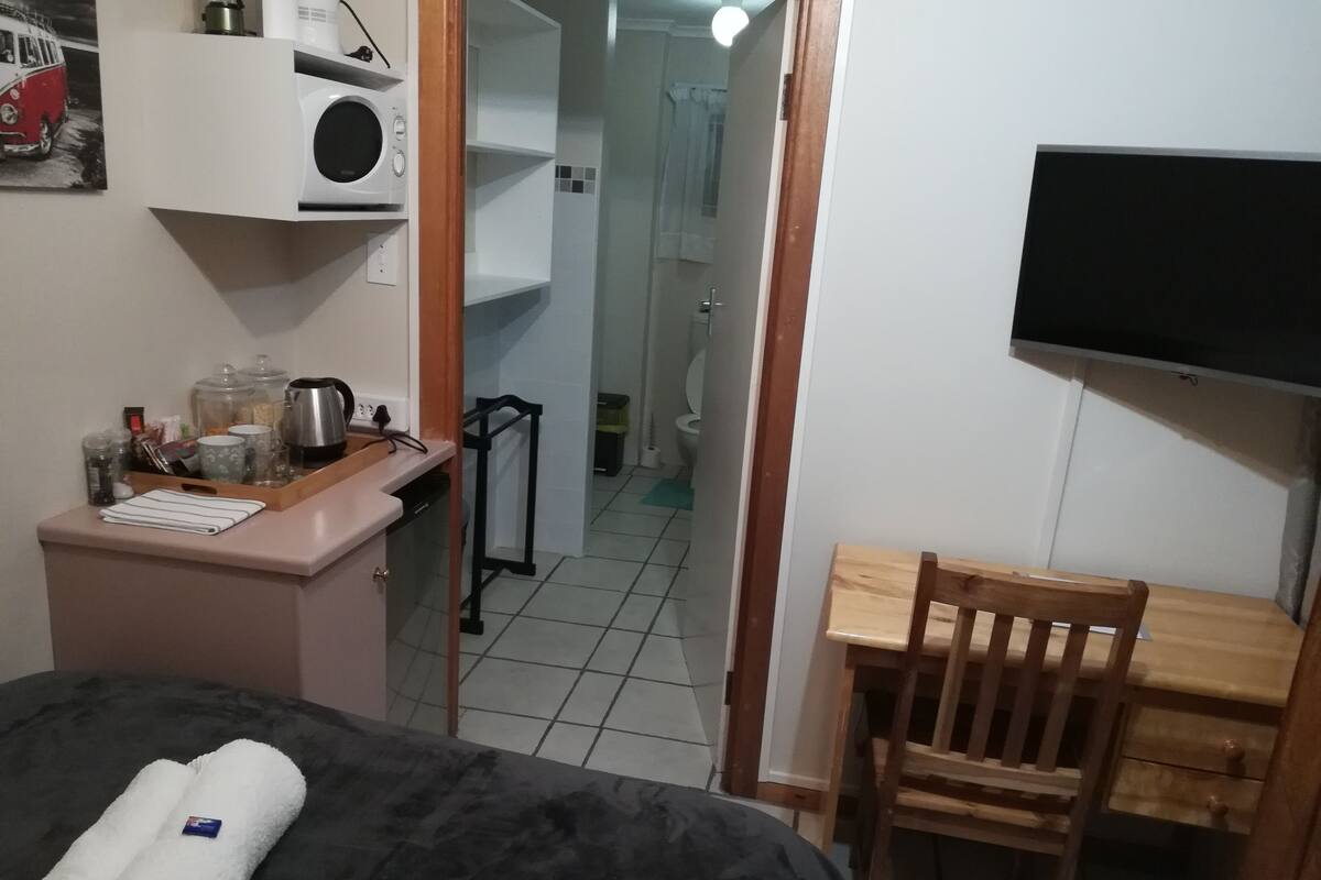 A small, compact room with a bed, a desk, a chair, a microwave, and a television.