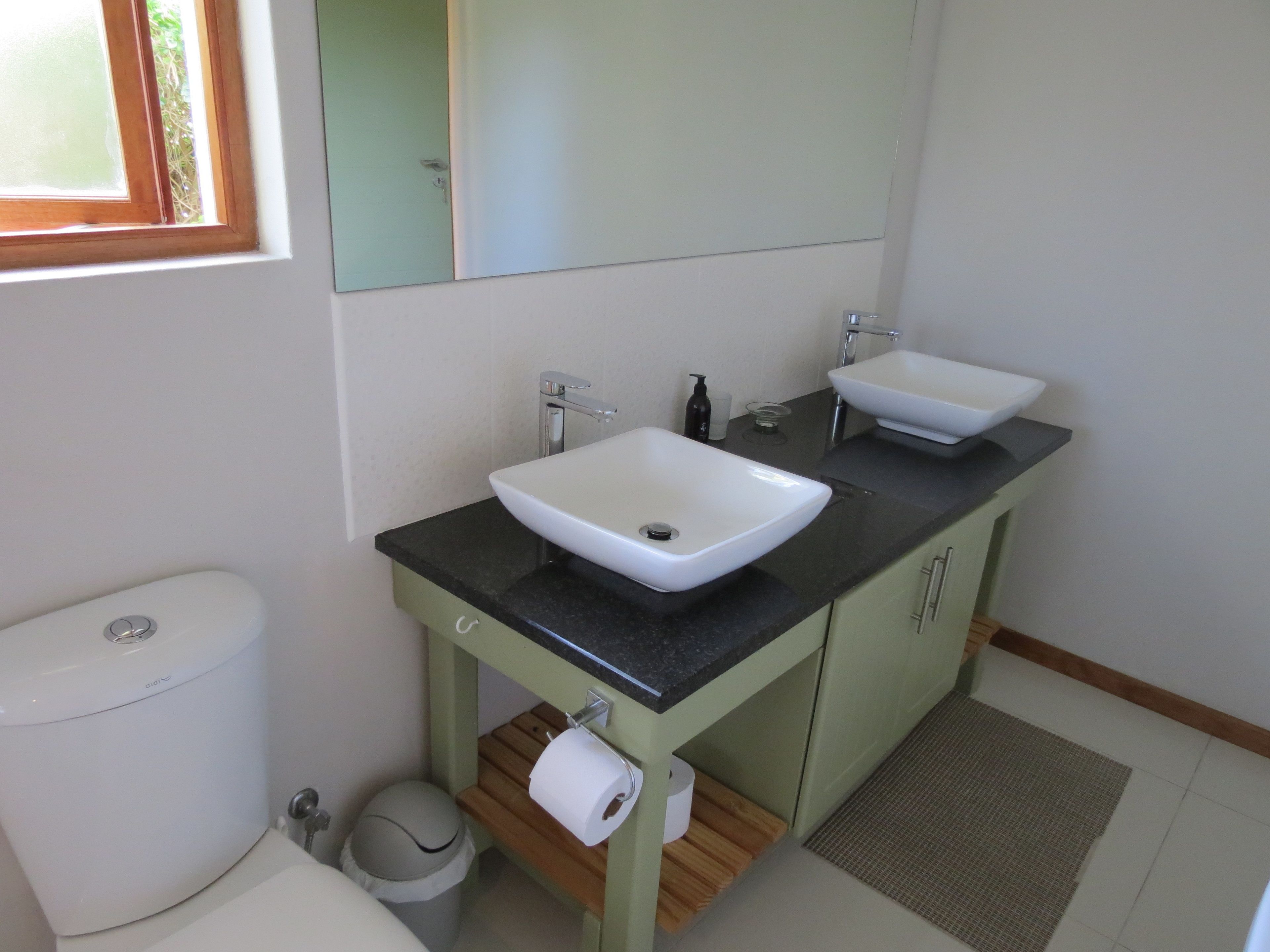 A bathroom with two sinks, a toilet, and a mirror.