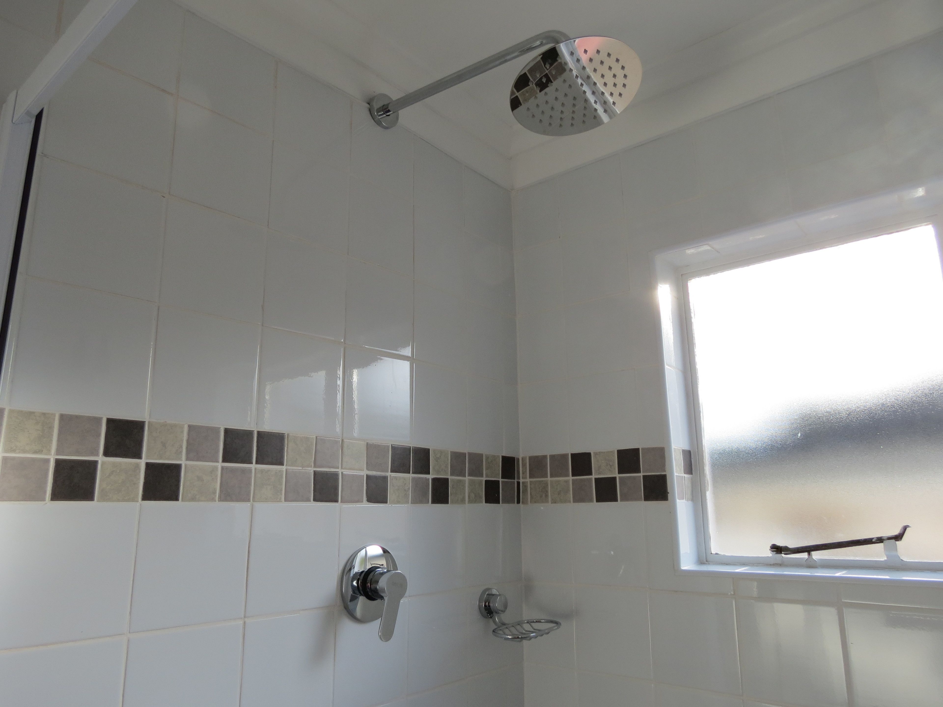 A bathroom with white tiles, a showerhead, a window with a view, and a towel rack.