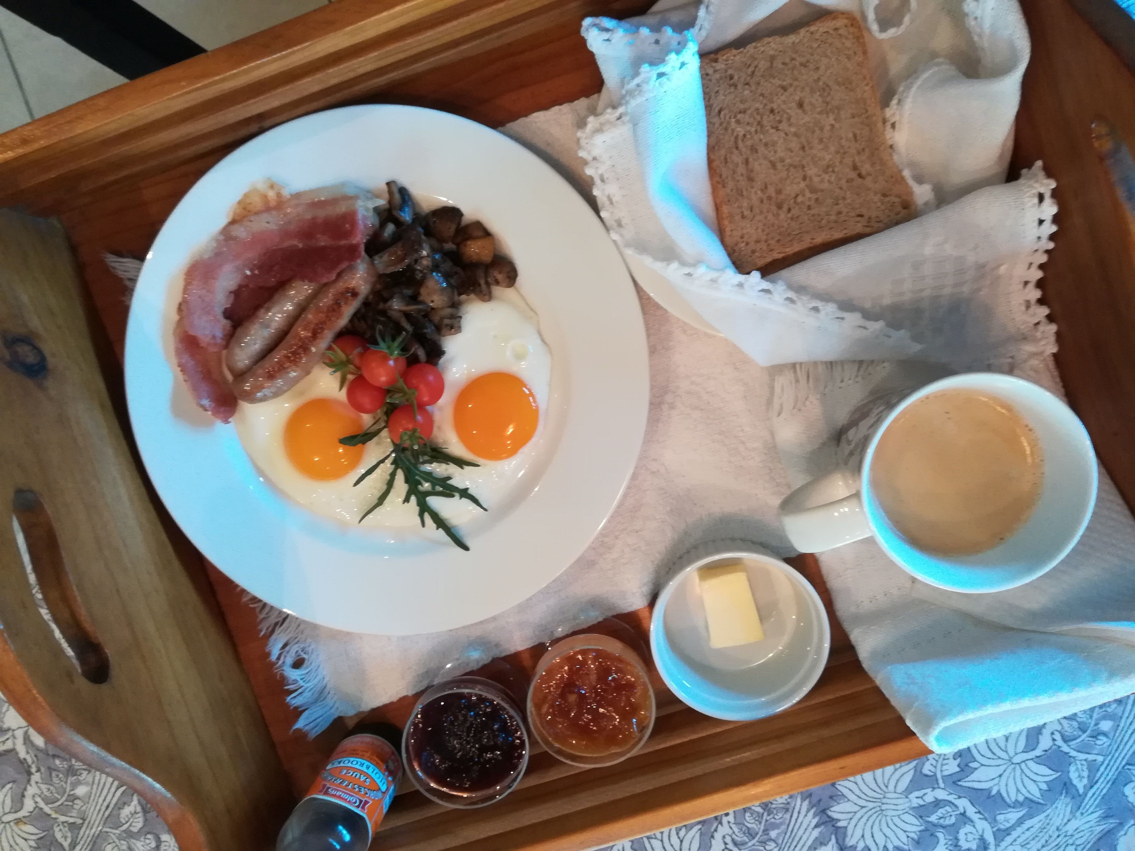 Ontbijtbakje met eieren, spek, champignons, toast, boter, jam en een kop koffie.