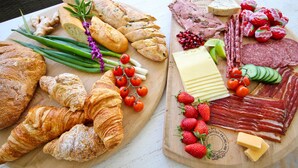 Ein Holzbrett mit verschiedenen Lebensmitteln, darunter Brot, Käse und Wurstwaren.
