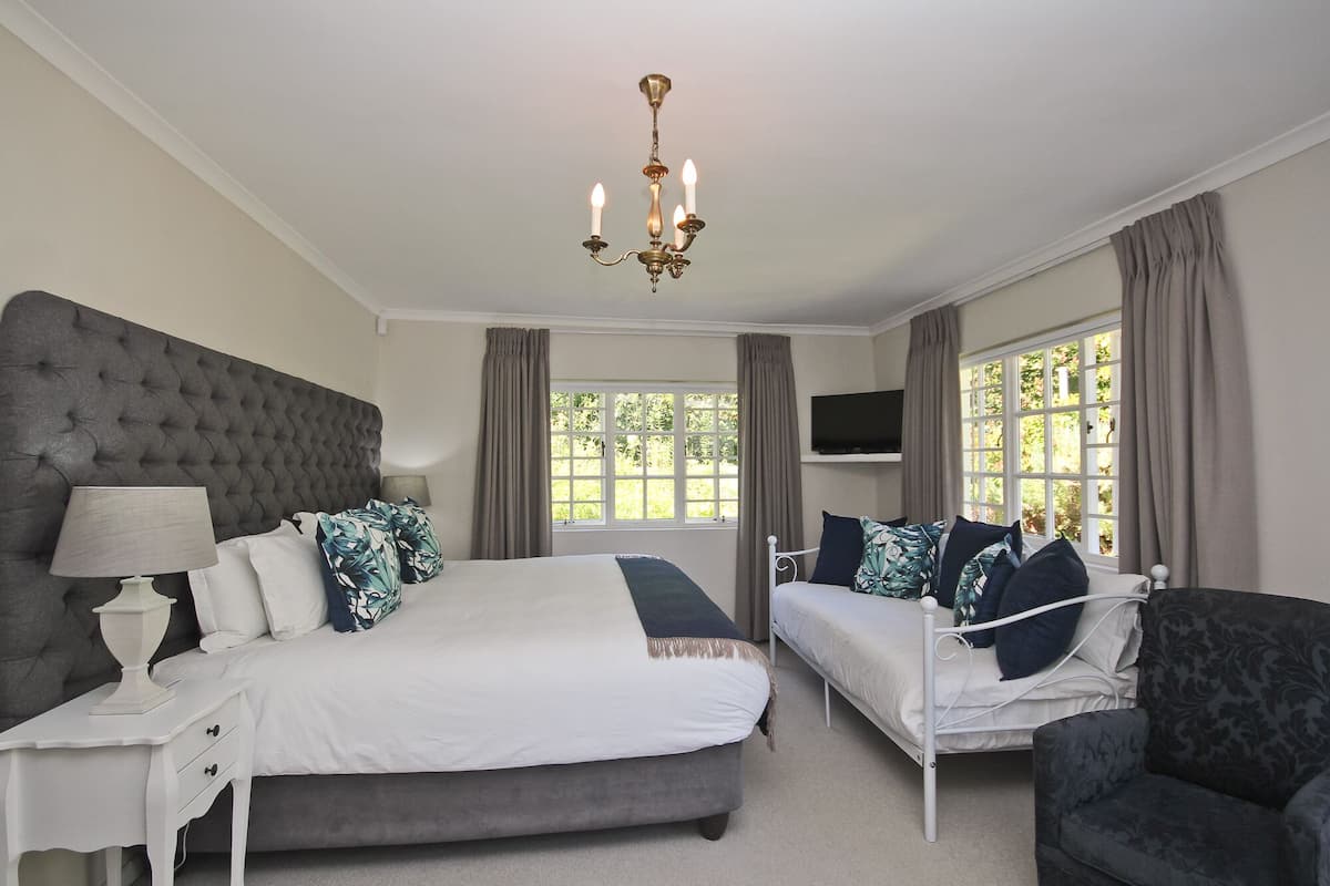 A bedroom with a large bed, a smaller bed, a chair, a TV, and a chandelier.