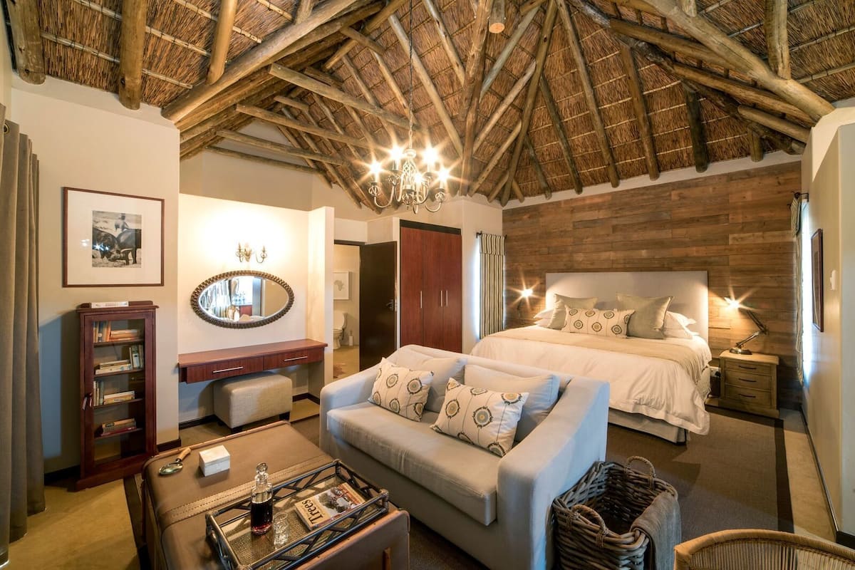 Een gezellige slaapkamer met een groot bed, een zithoek met een bank, een houten garderobe en een spiegel.