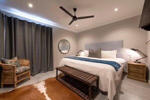 Ein Schlafzimmer mit einem Bett, Nachttischen, einem Deckenventilator, einem runden Spiegel, einer Bank und einem Kuhfellteppich.