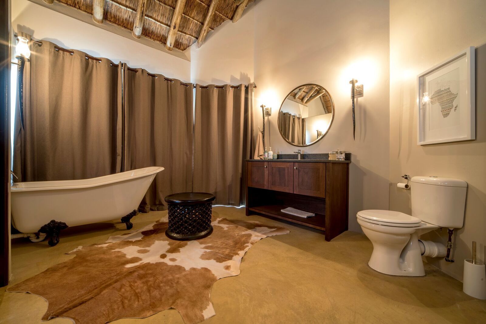 A bathroom with a bathtub, a toilet, a vanity with a mirror, and a cowhide rug.