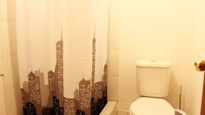 A bathroom with a toilet, a shower curtain with a cityscape design, and tiled walls. - Casa Sirius (San Pedro de Atacama)