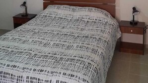 A bedroom with a wooden bed, a white patterned bedspread, two bedside tables with lamps, and a framed abstract artwork on the wall. - Casa Sirius (San Pedro de Atacama)