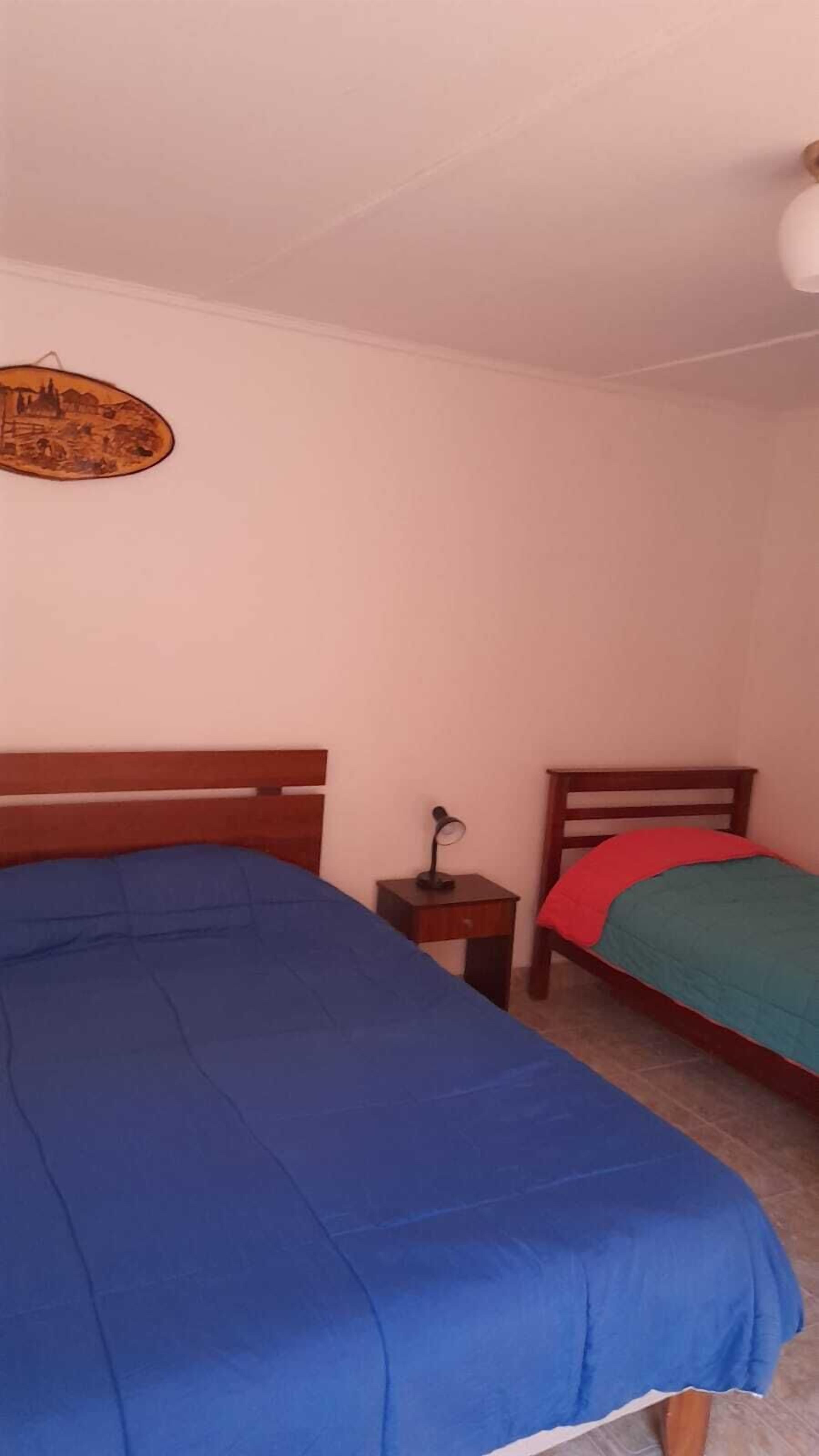 A bedroom with two beds, a nightstand, a lamp, and a wall hanging.