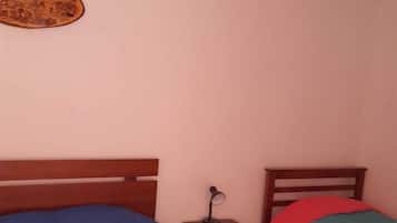 A bedroom with two beds, a nightstand, a lamp, and a wall hanging.