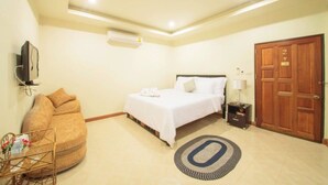 A hotel room with a bed, a sofa, a TV, an air conditioner, a wooden door, and a small table with a lamp. - Banter Resort (Buriram)