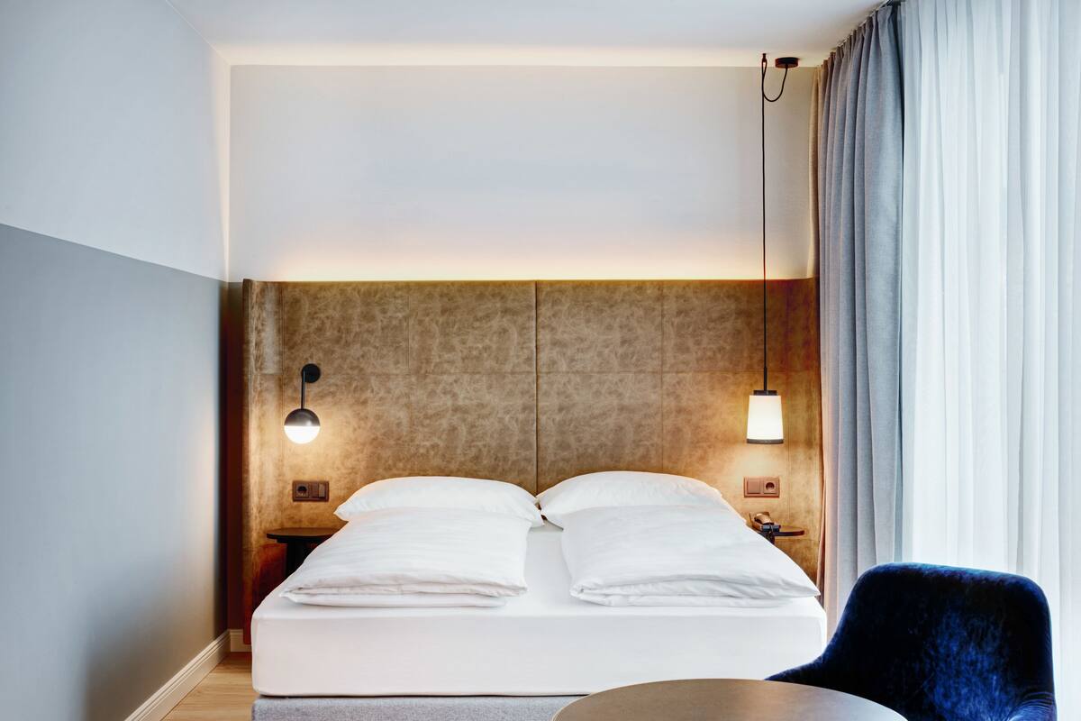 Een moderne hotelkamer met een bed, nachtlampjes, een ronde tafel en een stoel.