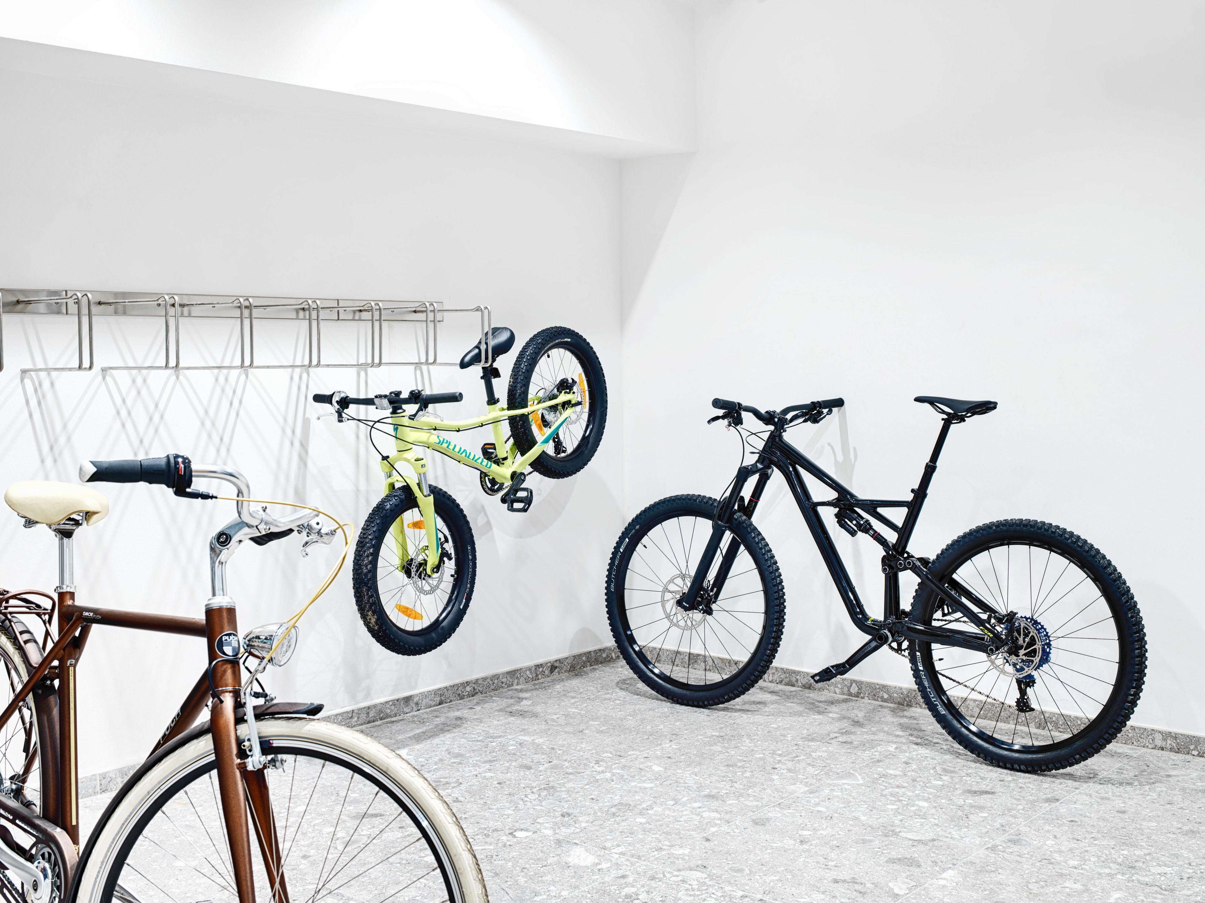 A room with bicycles, a wall-mounted bike rack, and a concrete floor.