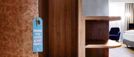 Une chambre d’hôtel avec une armoire en bois, une étiquette bleue accrochée au mur, un lit, une chaise et une table de chevet.