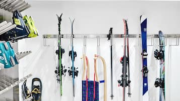 A ski equipment storage area with skis and snowboards hanging on a rack, and a pair of snowshoes on the floor.