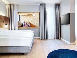 Una habitación de hotel moderna con una cama grande, un televisor de pantalla plana, un cuadro en la pared y piso de madera.